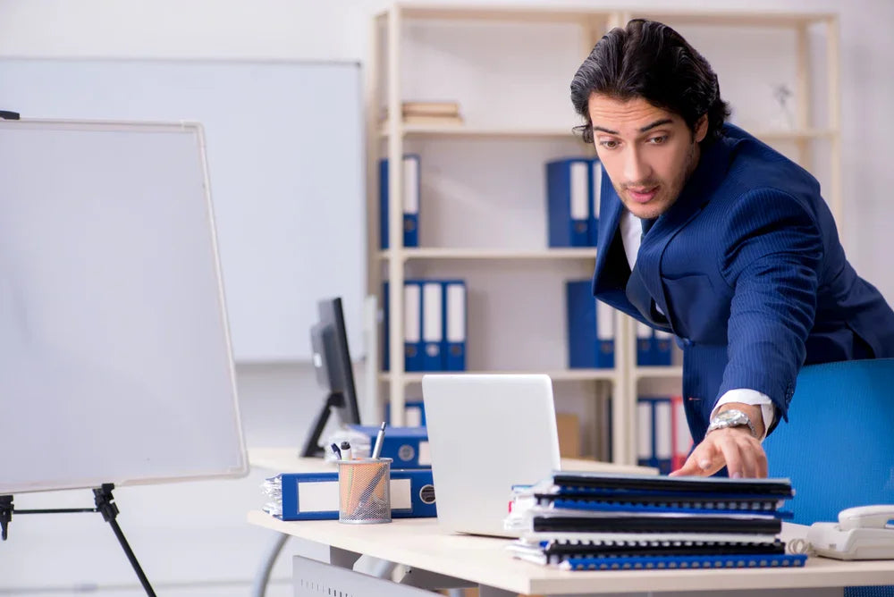Uomo in giacca e cravatta in ufficio afferra dei documenti in maniera furtiva e frettolosa commettendo furto di beni aziendali o dati sensibili.