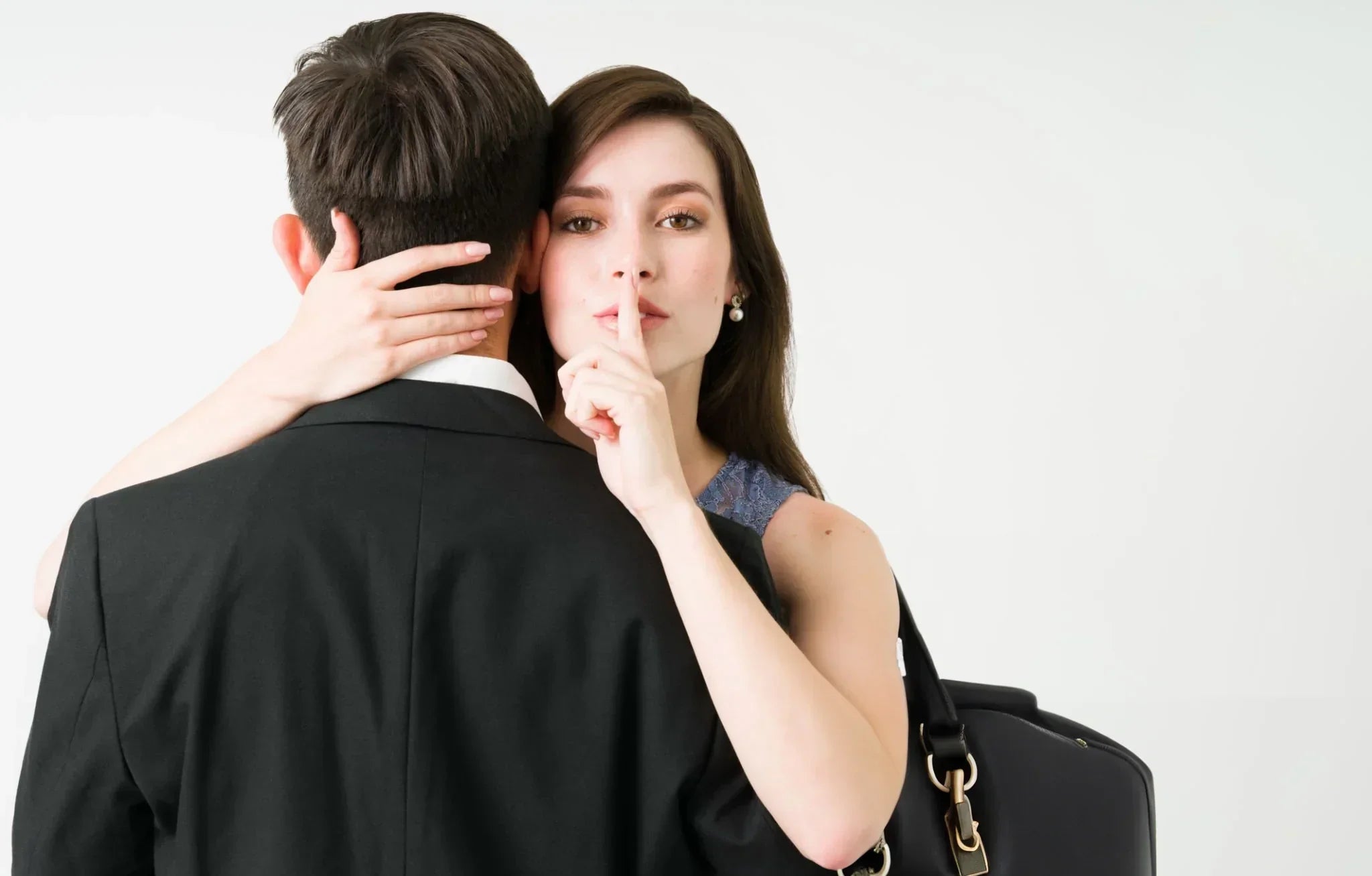 Donna abbraccia uomo e fa segno di silenzio con dito indice davanti alla bocca, simbolo di indagini per infedeltà coniugale.