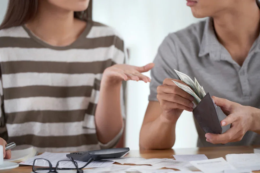 Giovane donna pone la mano in segno di richiesta di denaro al giovane ragazzo accanto a lei che estrae denaro dal proprio portafogli. Simbolo di richieste economiche sospette prima del matrimonio.