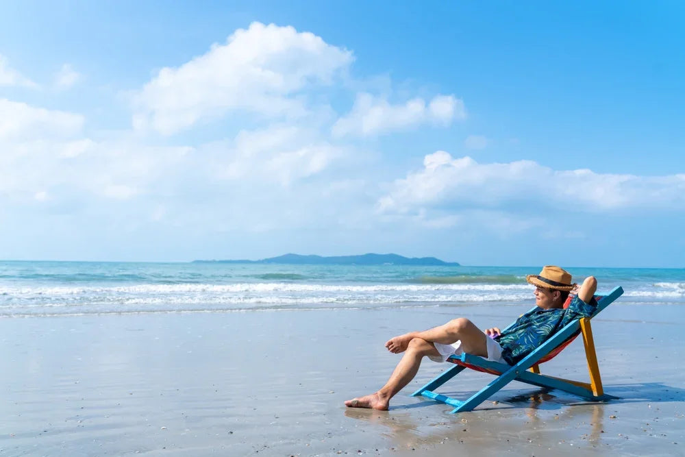 Uomo con camicia a fiori e cappello accomodato su uno sdraio in riva al mare, simbolo di uso improprio della Legge 104 per agenzia investigativa.