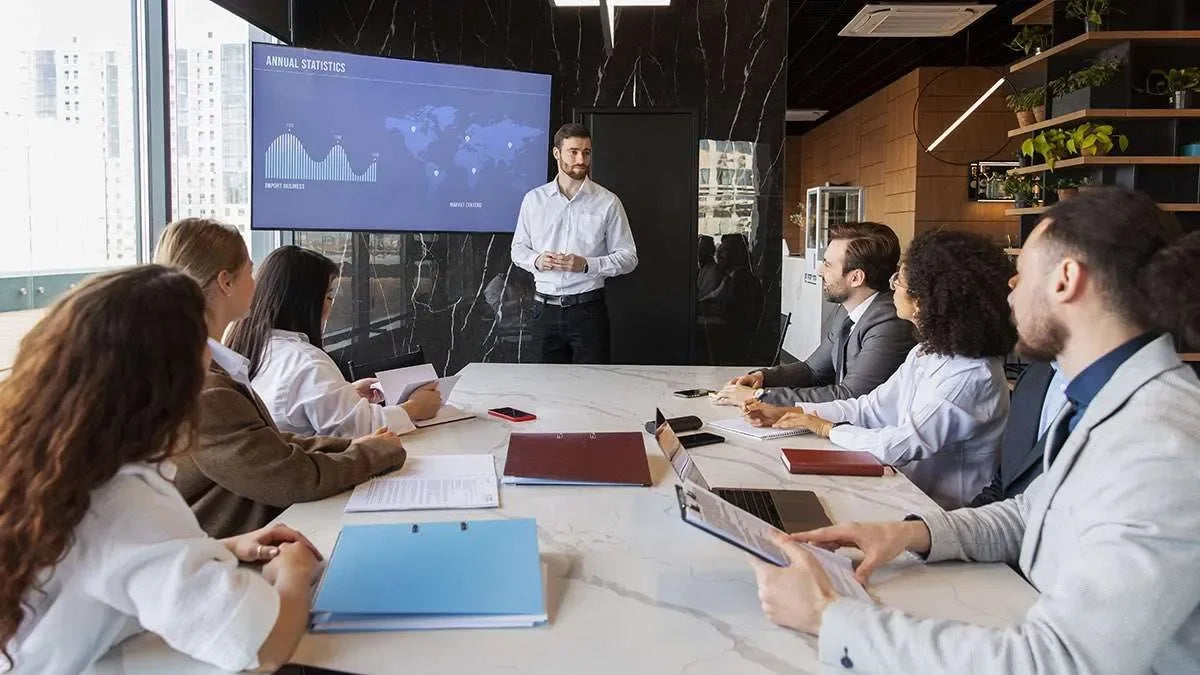 8 investigatrici e investigatori privati seduti ad un tavolo in riunione in un ampio studio fornito di schermo, computer e documentazione.