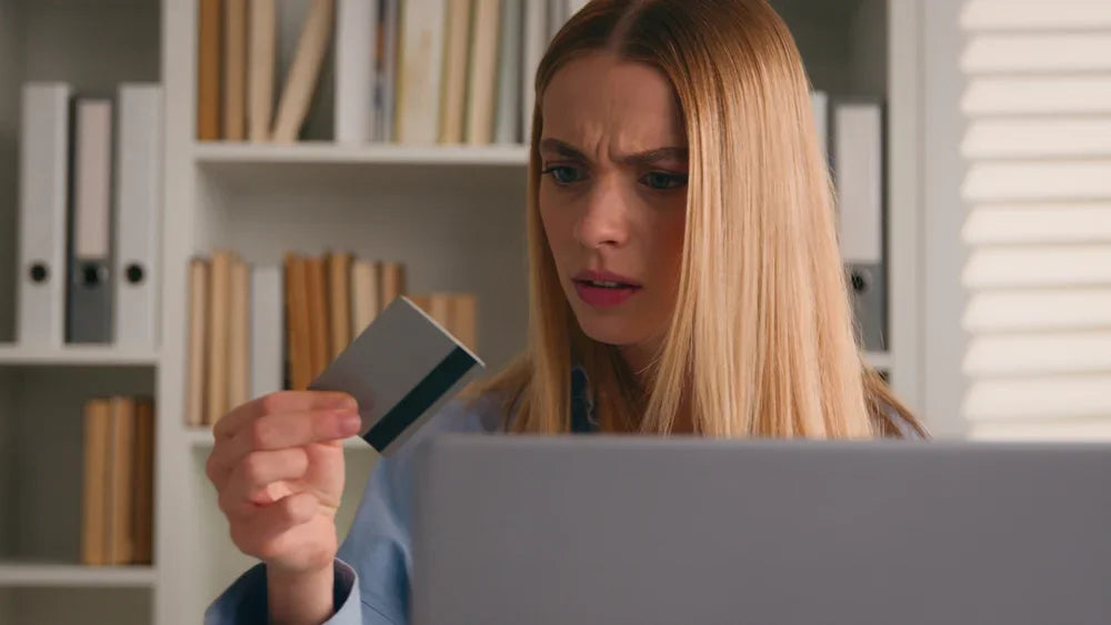 Donna guarda la carta di credito che ha in mano con espressione perplessa. L' ambientazione è in ufficio davanti ad un computer. Simbolo di indagini aziendali prima di prestiti personali o dilazioni di pagamento.