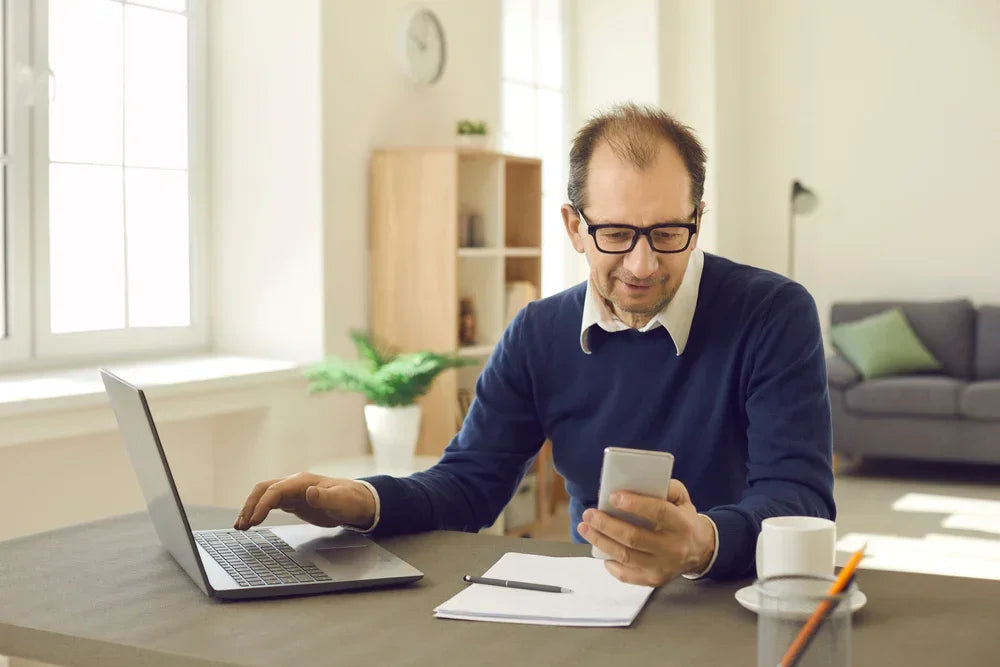 Uomo al telefono guarda il telefono invece di lavorare, simbolo di indagini aziendali per doppio lavoro e secondo impegno