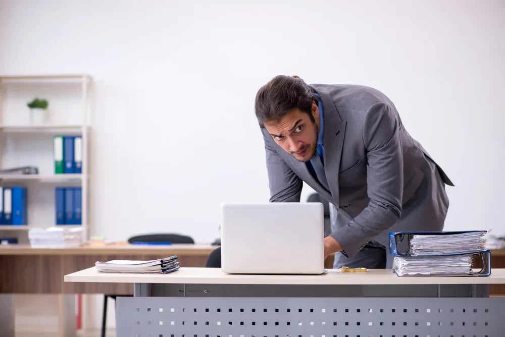 Uomo in ufficio agisce con sospetto davanti al computer, simbolo di sottrazione di dati aziendali riservati.