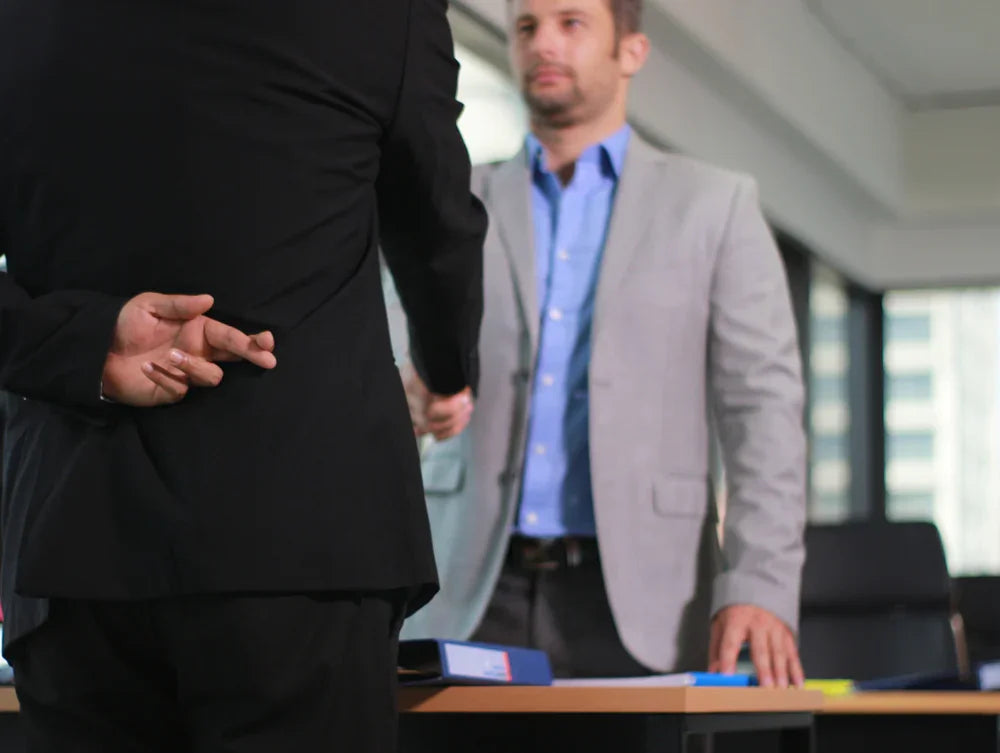 Stretta di mano tra due uomini, uno incrocia le dita dietro la schiena: referenze dubbie. Simbolo di indagini pre assunzione.