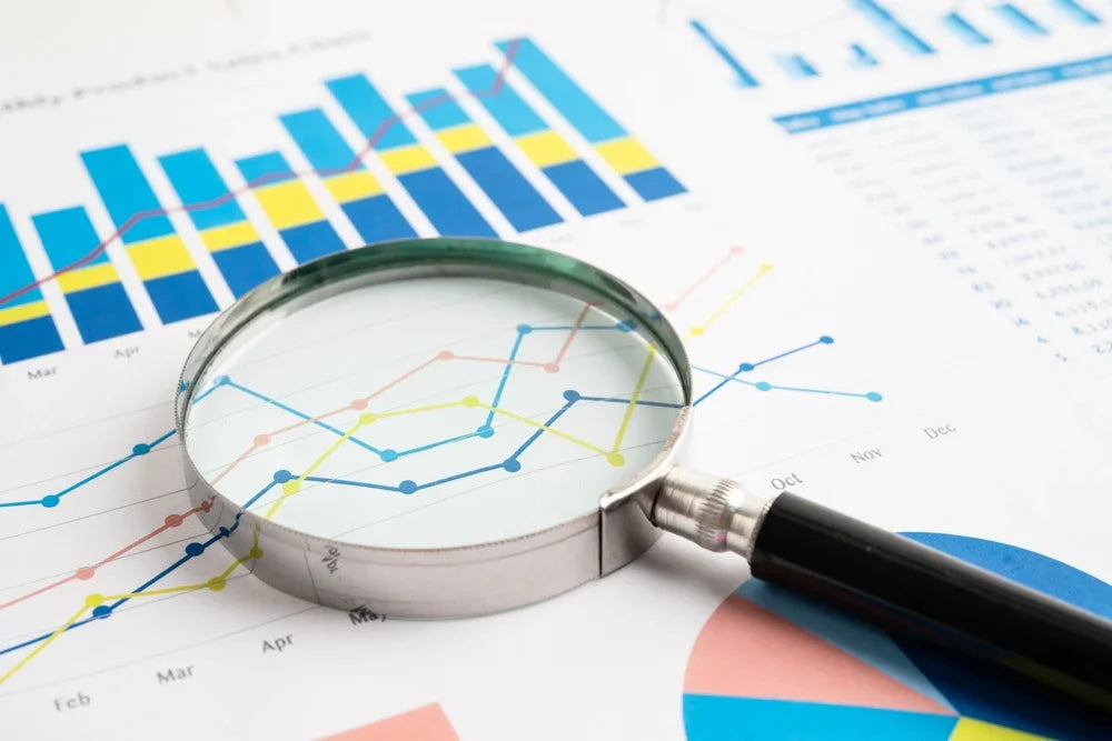 Lente di ingrandimento appoggiata su un foglio con grafici. Simbolo di crediti aziendali e frodi simulati.