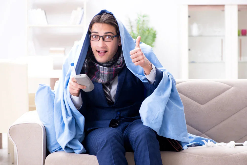 Uomo in giacca e cravatta con termometro in mano e trapunta fa il simbolo di okay con la mano, simbolo di dipendente in falsa malattia svolge altre attività.