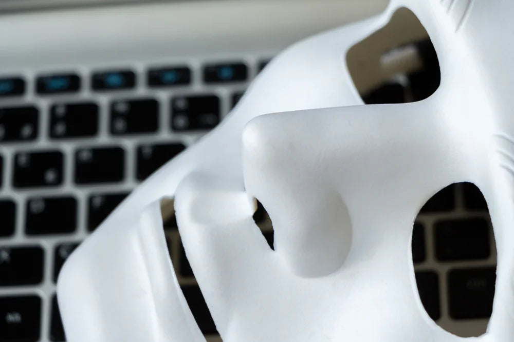 Maschera bianca su tastiera laptop, simbolo di identità false, truffe online e indagini OSINT.