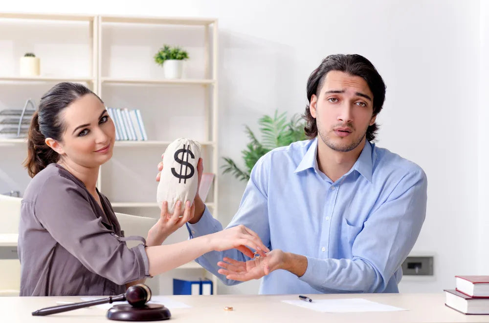 Uomo con espressione triste e donna con espressione soddisfatta si scambiano sacchetto con icona dei soldi e anello nuziale. Simbolo di indagini patrimoniali.