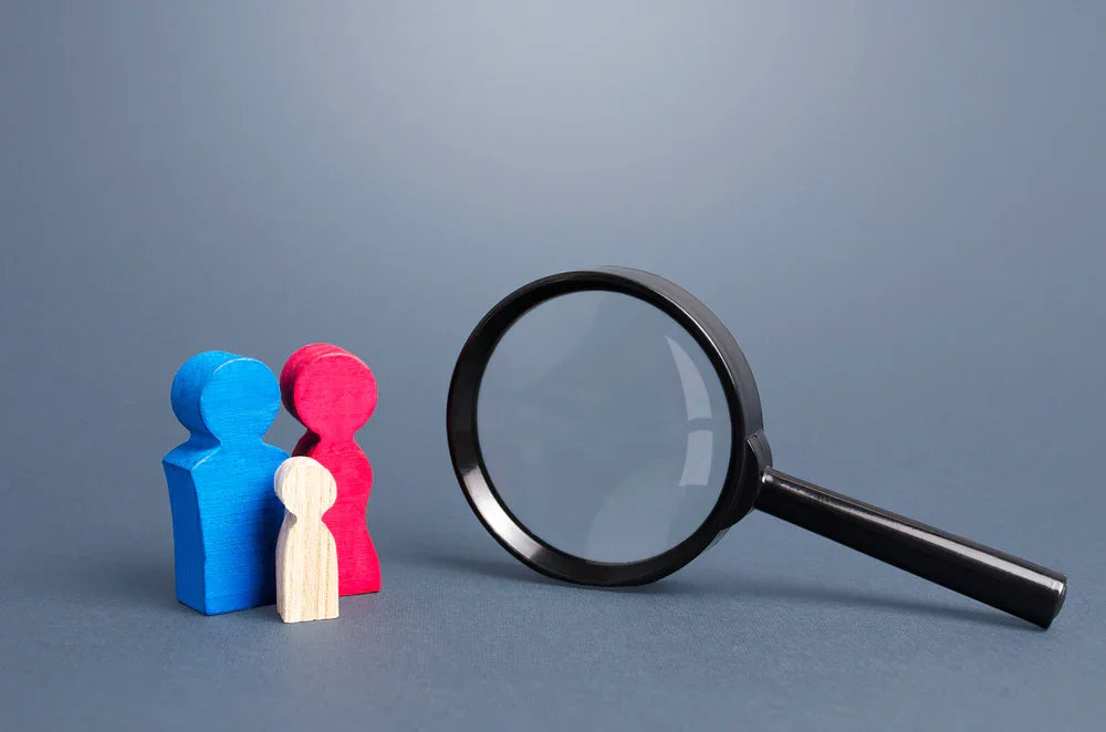 Lente di ingrandimento da investigatore privato, con miniatura di una famiglia. Simbolo di monitoraggio genitore affidatario.