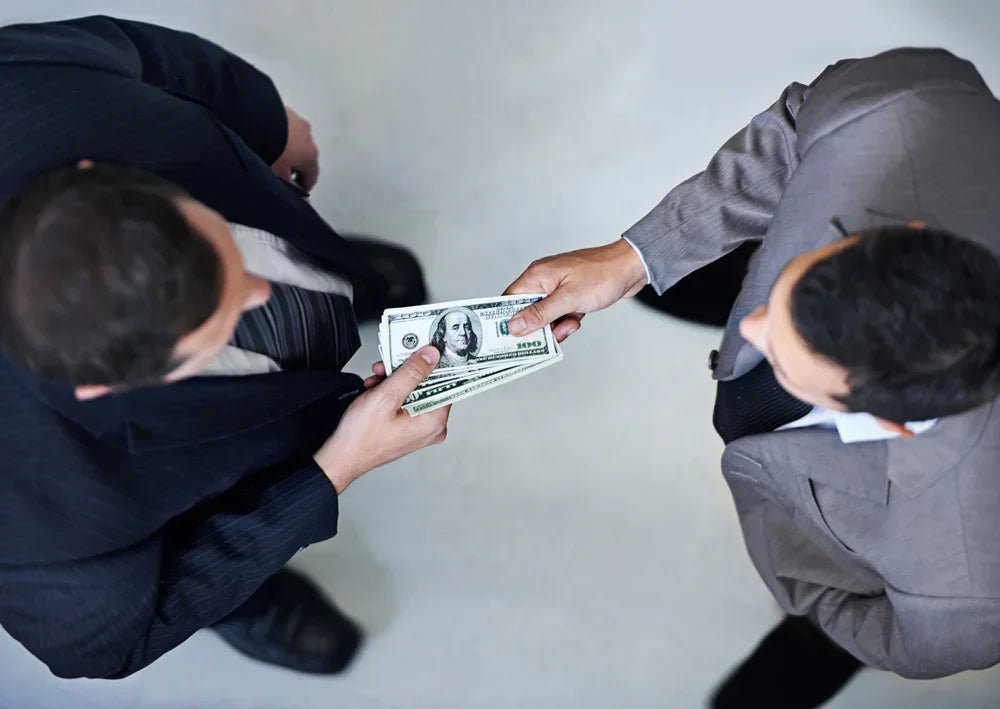 Scambio di denaro tra due uomini in abiti eleganti, simbolo di redditi o attività lavorative non dichiarate.